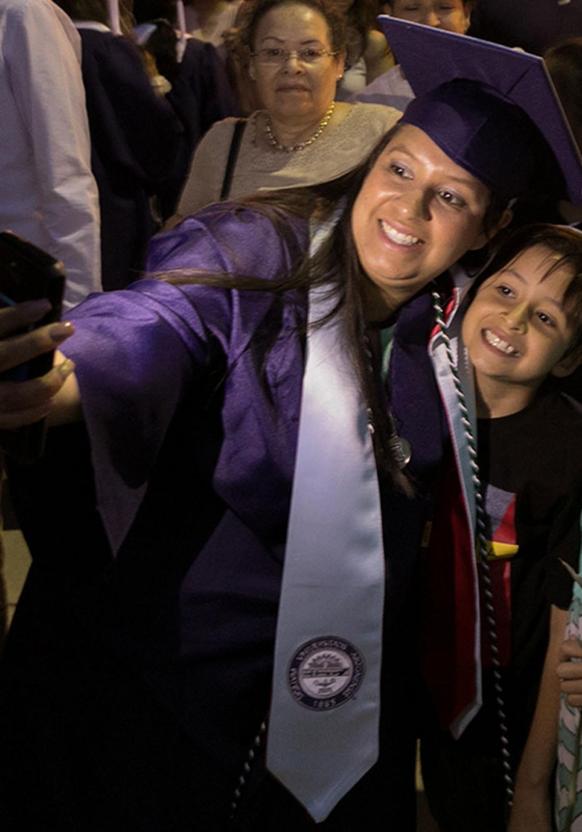 Photo of a student posing with their sibling as they both take a selfie on graduation day