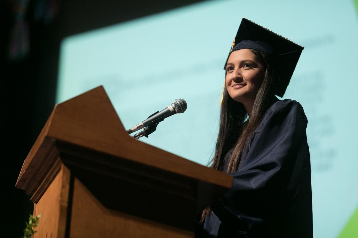 A student is speaking on stage at a podium looking inspirationally with a smile at the crowd in Centennial Hall for the Guerrero Center Convocation